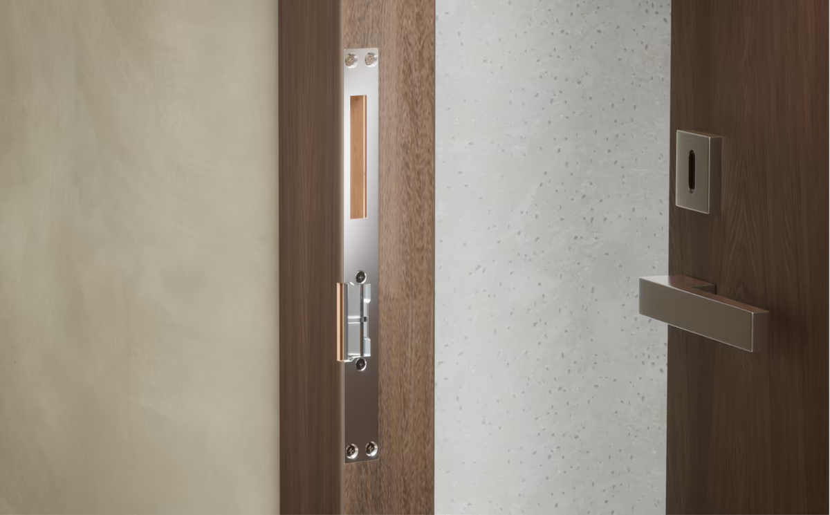 Ubiquiti UACC-Lock-Strike-Secure-8mm UniFi Narrow 8mm Fail-Secure Strike Lock installed with the long front plate in a timber door frame beside an open door.