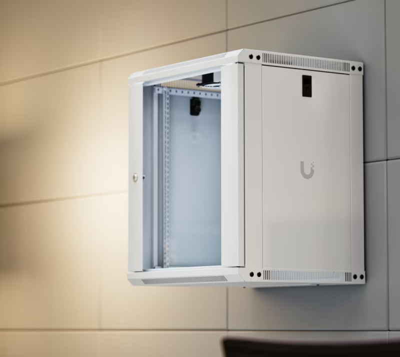 Ubiquiti UACC-Rack-12U-Wall-450-G UniFi Slim 12U network cabinet installed on an office wall, showing its compact profile, ventilated frame and lockable side panel.