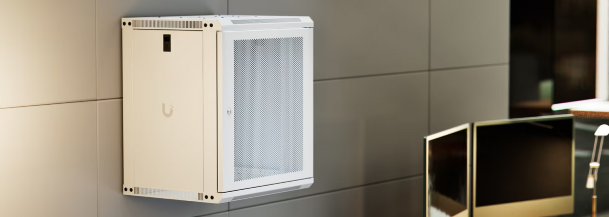 Ubiquiti UACC-Rack-12U-Wall-450-P UniFi Slim 12U rack cabinet wall-mounted beside computer monitors in a modern office workspace.