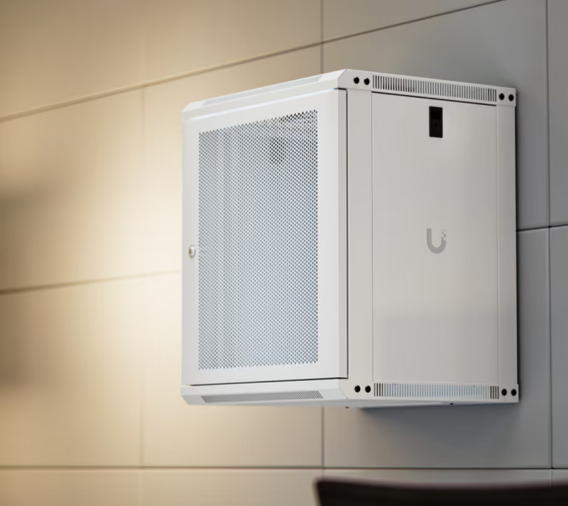 Wall-mounted Ubiquiti UACC-Rack-12U-Wall-450-P UniFi Slim 12U rack cabinet in an office, showing the perforated door, solid side panel and ventilation.