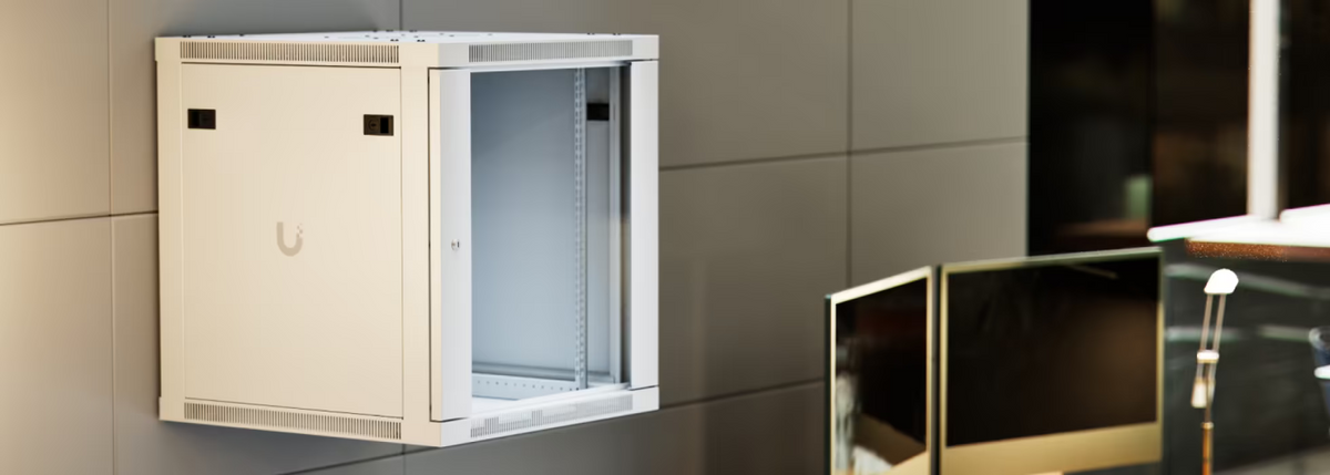Ubiquiti UACC-Rack-12U-Wall-600-G UniFi Standard 12U rack cabinet wall-mounted in a modern office, showing the glass front door, lockable side panel and interior mounting rails.