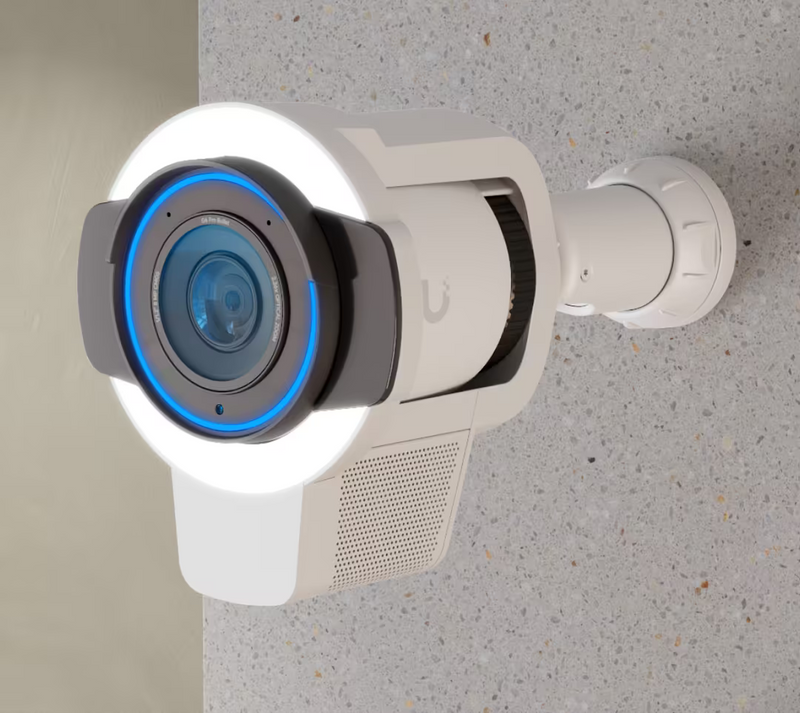 Ubiquiti UACC-Pro-Bullet-Enhancer UniFi Pro Bullet Enhancer in white installed with a UniFi bullet camera on a concrete wall, illuminated LED floodlight and blue status ring