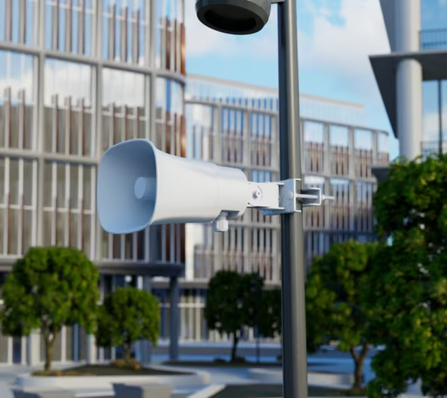 White Ubiquiti UP-AI-Horn-Speaker mounted outdoors on a pole beside a commercial building